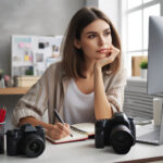 A-young-woman-aged-18-35-sitting-at-her-desk-with-a-laptop-open-and-a-computer-screen-beside-he